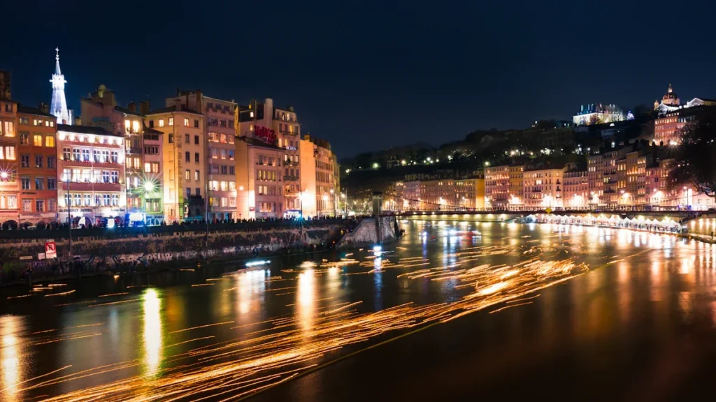Night view of a European riverside city with glowing lights reflecting on water.