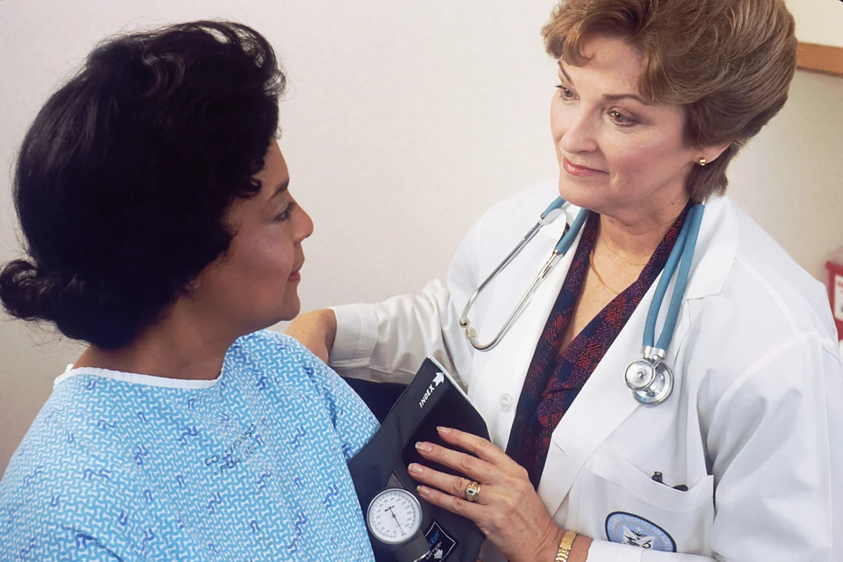 A female doctor in a white coat measures a patient's blood pressure in clinic.