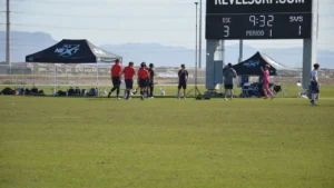 Soccer referees in red shirts standing on a field near a digital scoreboard.
