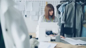 Young female clothing designer working on a sewing machine in a creative studio.