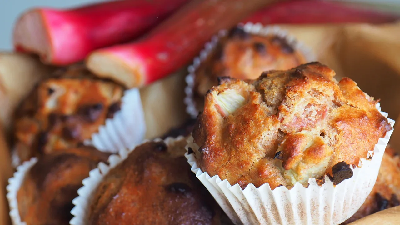 Close-up of freshly baked rhubarb muffins in a bowl with fresh rhubarb stalks.
