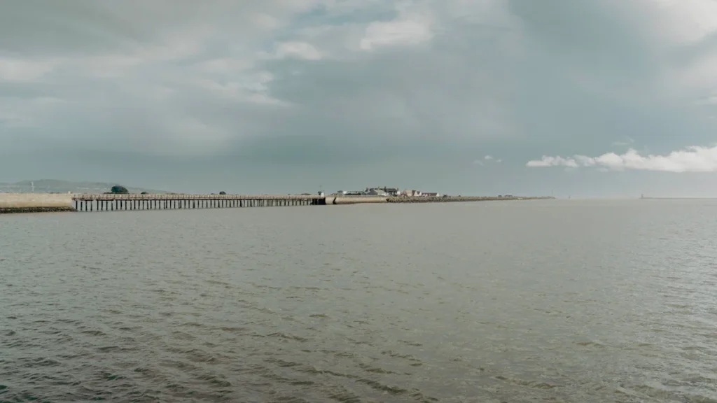Distant view of a coastal pier and harbor buildings under a cloudy sky.