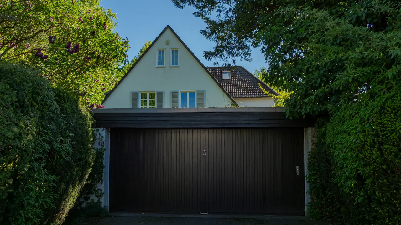A suburban house with a large dark garage door in a quiet neighbourhood.