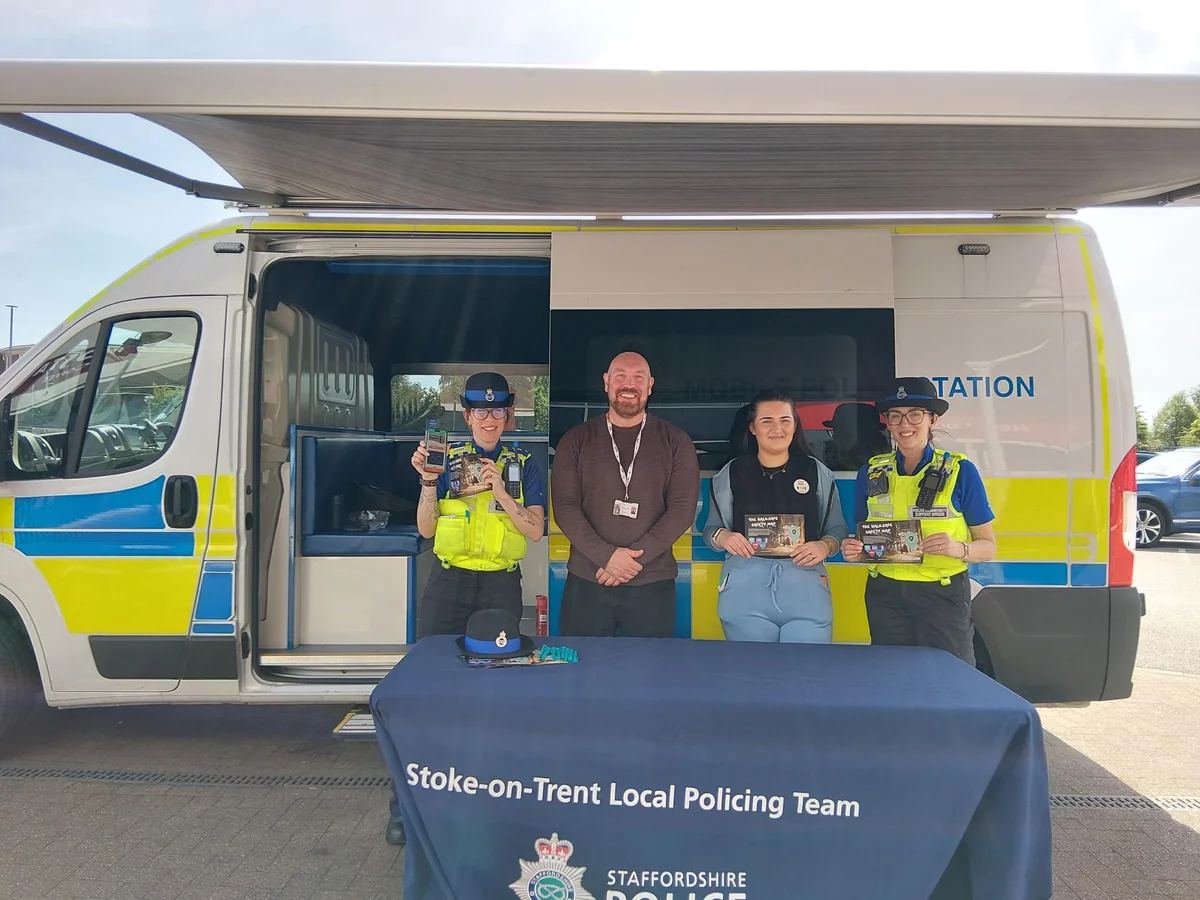 Two police officers and two civilians stand before a Staffordshire Mobile Police Station van.