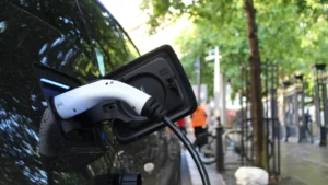 An electric car charging on a residential street with green trees in the background.