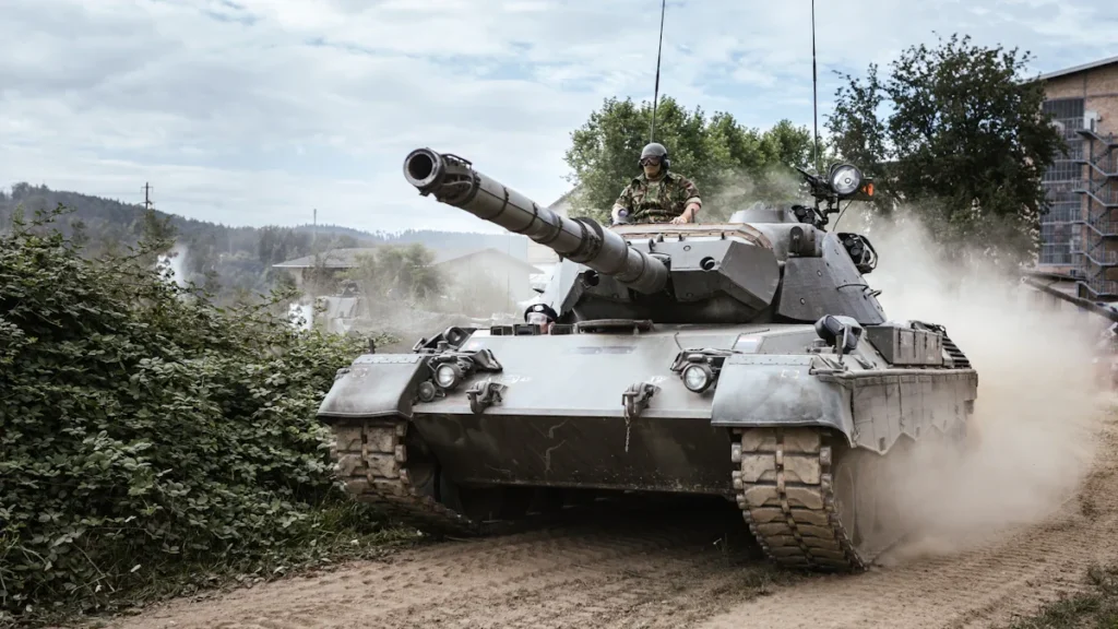 Military battle tank moving across a green grass field during the day.